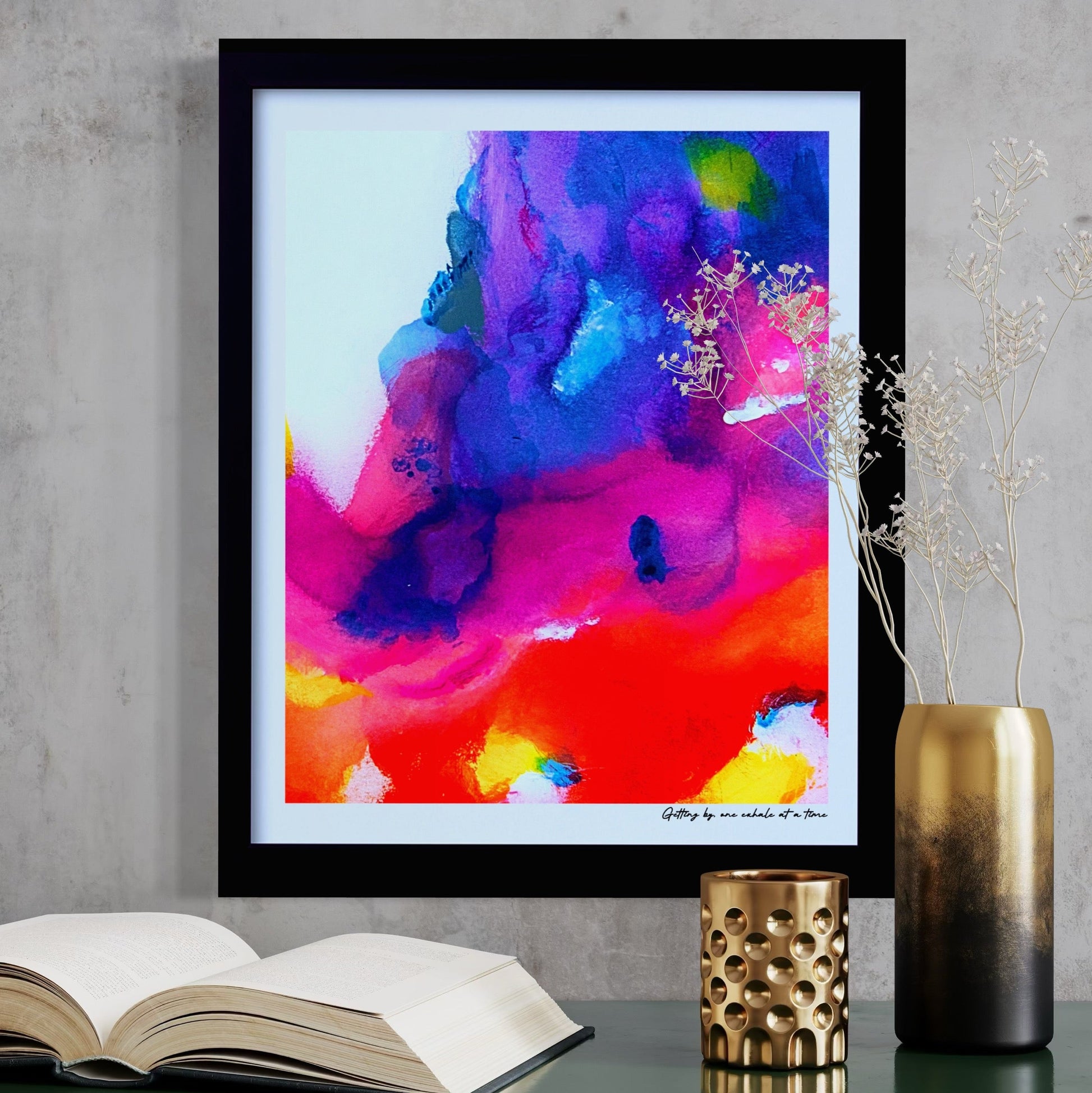 Framed abstract artwork with a colorful design on a wall above a green surface with books and decorative items.
